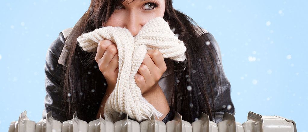 Female with with winter clothing sitting indoors with a portable heater